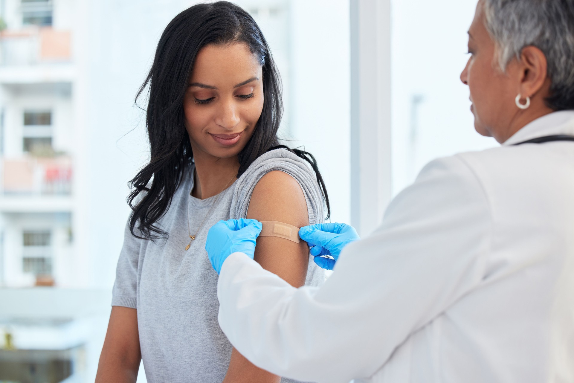 Healthcare, woman and doctor with plaster, vaccination and consultation in a hospital, cure and disease. Female patient, client and medical professional with care, vaccine and injection for safety